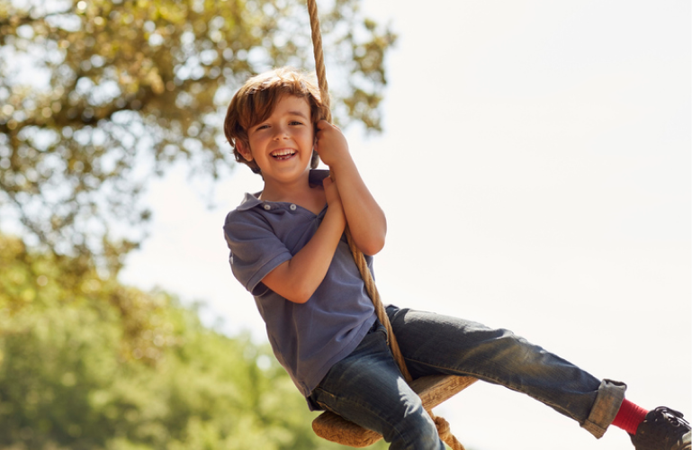 kid smiling and swinging from a rope swing