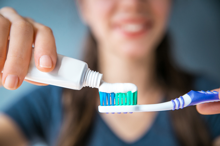 Close Up Of Smiling Young Woman Putting Toothpaste On Her Toothbrush