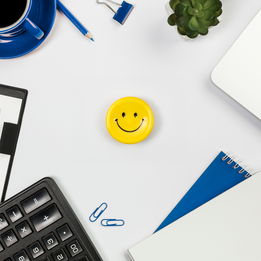 Spiral Notebook And Smiley Face Pin With Paperclips Sitting On Desk