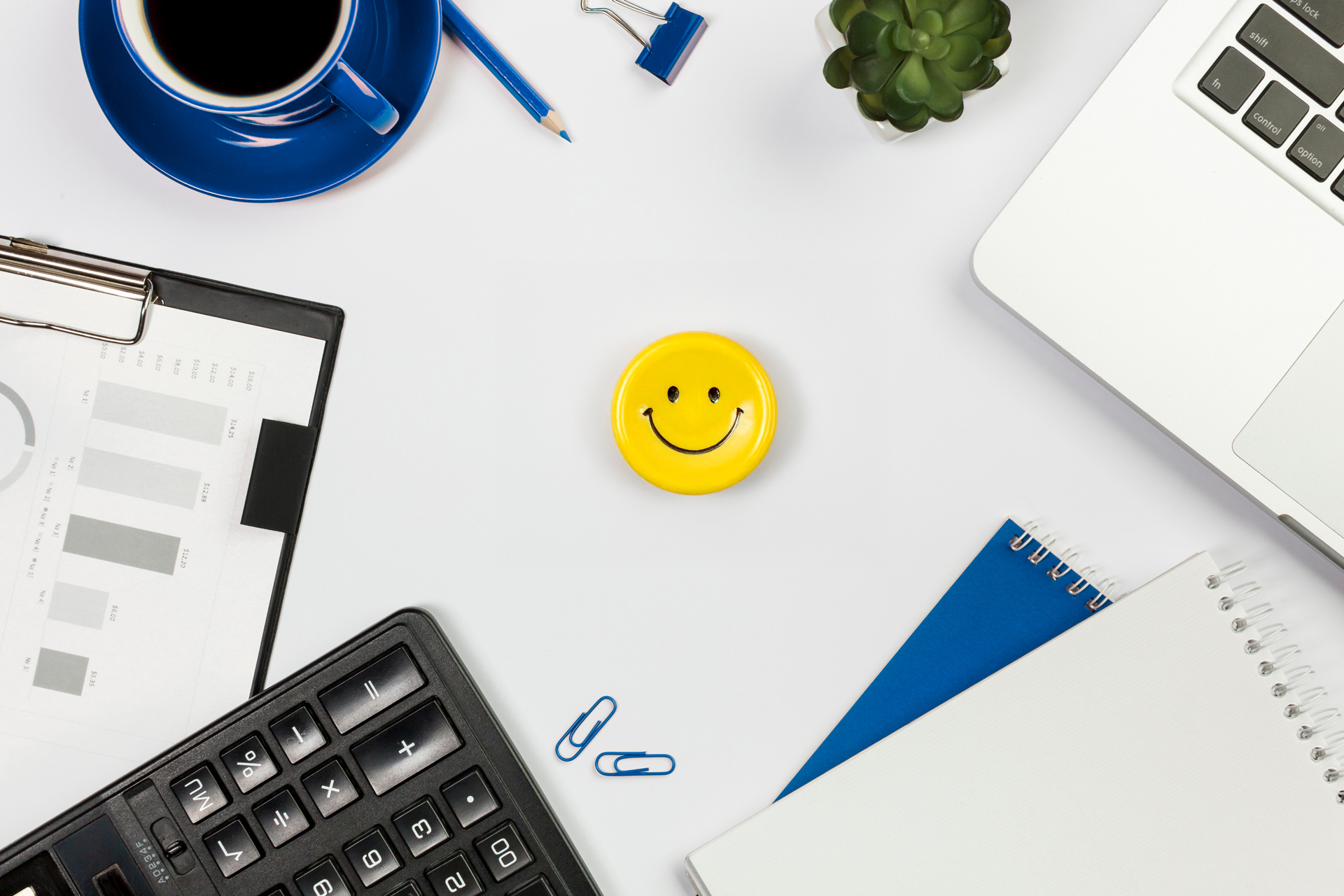 Spiral Notebook And Smiley Face Pin With Paperclips Sitting On Desk