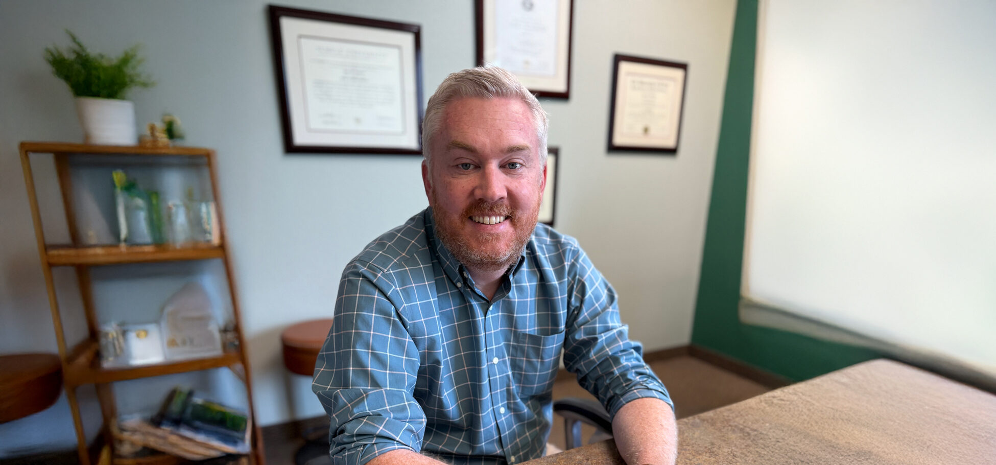 Cleburne, TX orthodontist Dr. Jason Tennison at his desk in a blue and white plaid button up