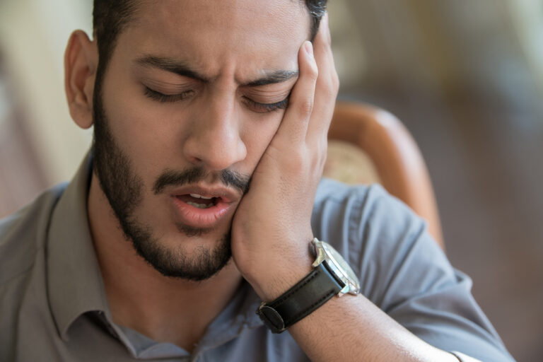 Man sitting down and holding the side of his of his face in pain